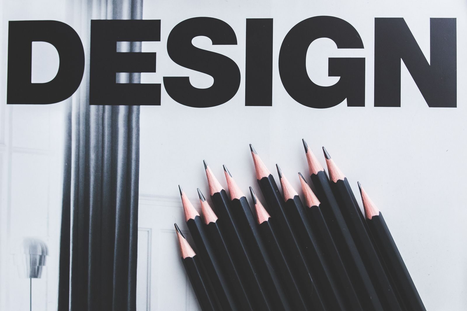 Black pencils arranged creatively next to large typography 'DESIGN'.